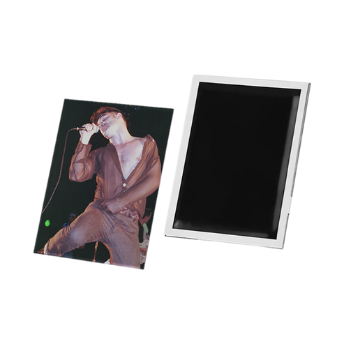 A rectangular photo magnet or printed magnet shown from two angles on a plain white background: one side displays a printed photo of a performer in a brown outfit, and the other side shows a blank black surface with a white border.
