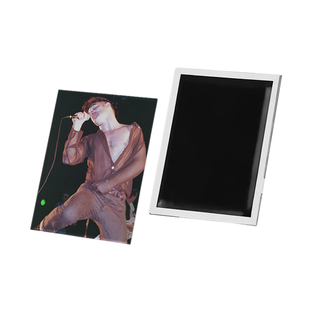 A rectangular photo magnet or printed magnet shown from two angles on a plain white background: one side displays a printed photo of a performer in a brown outfit, and the other side shows a blank black surface with a white border.
